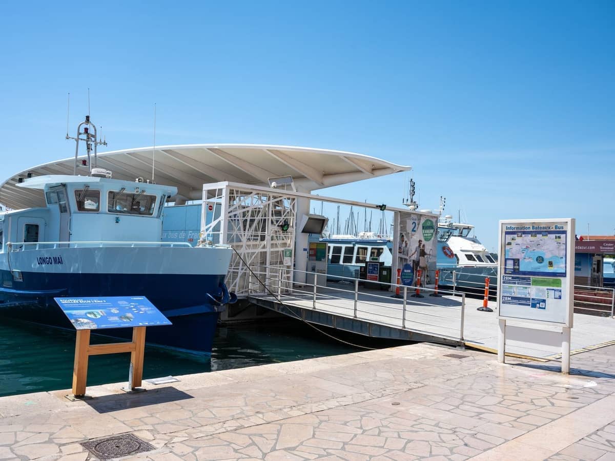 Modern ferry terminal in Ibiza with docked passenger ferries, informational signs, and clear blue sky.