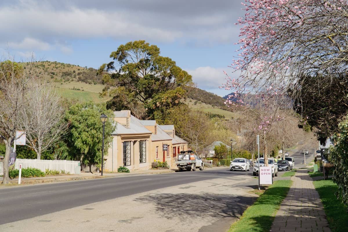 Historic street in Adelaide Hills with stone cottages, flowering trees and hillside scenery on a clear day.