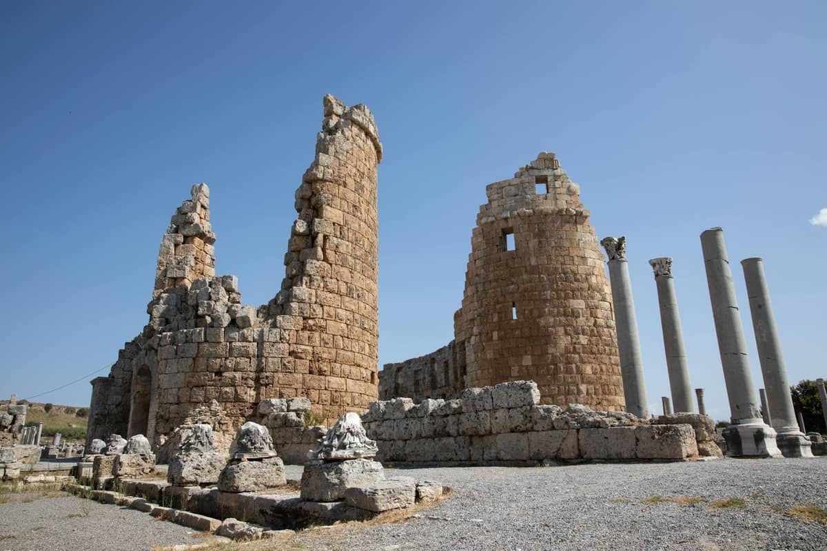 Ancient Roman stone towers and standing columns under a bright blue sky at a large archaeological ruin site.