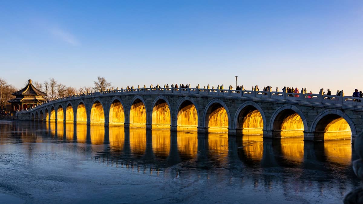 Il Ponte dei Diciassette Archi nel Palazzo d'Estate di Pechino, con la luce del tramonto che illumina gli archi e un padiglione tradizionale nelle vicinanze.