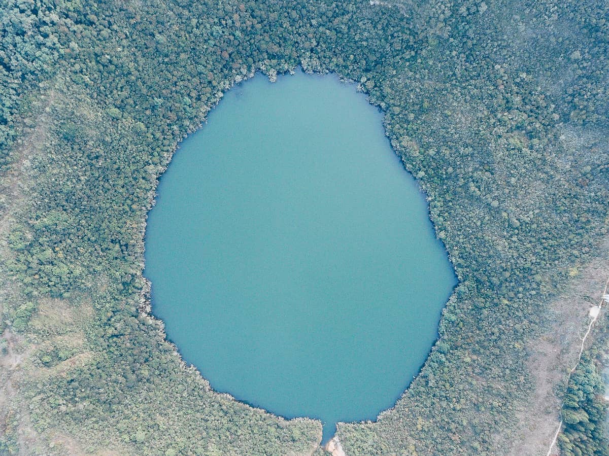 Aerial view of the nearly perfect circular crater of Laguna de Guatavita surrounded by dense forested hills.
