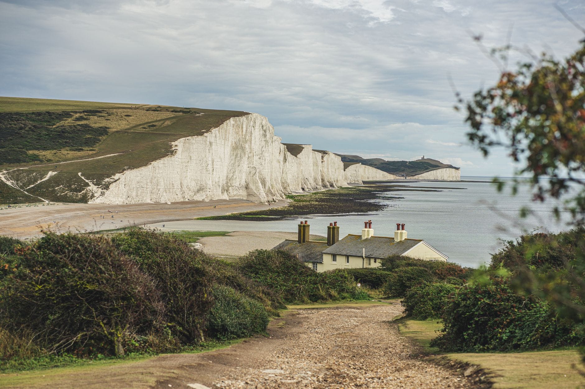 Dramatischer Blick auf die weißen Kreidefelsen der Seven Sisters mit Häuschen auf den Klippen, grünen Hügeln und Strand im South Downs National Park.
