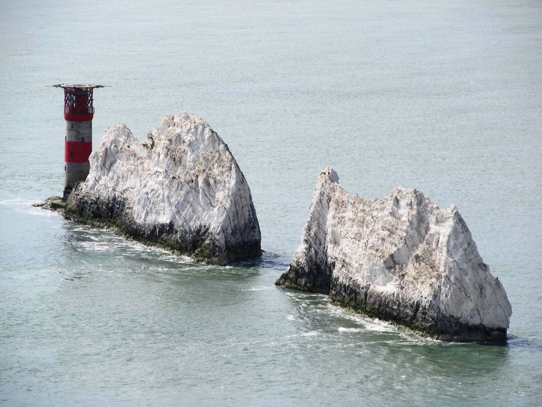Ikonische Kreidefelsen, bekannt als The Needles, mit einem rot-weißen Leuchtturm vor der Küste der Isle of Wight.
