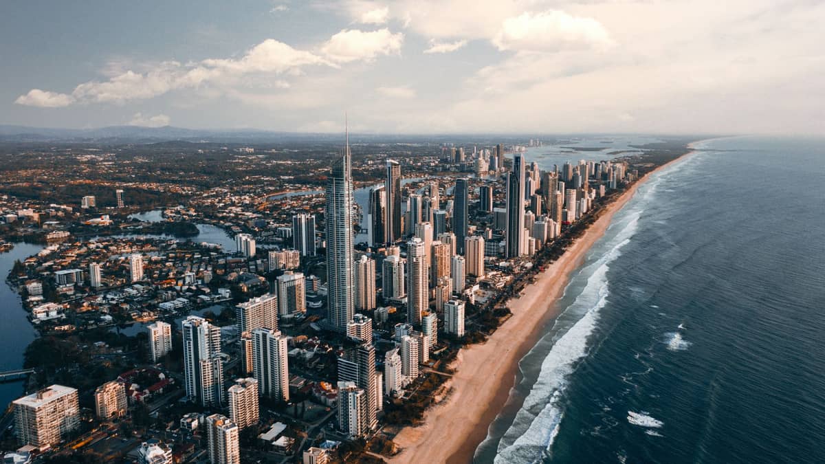 Luftaufnahme von Gold Coast mit Hochhäusern entlang des langen Sandstrandes, blauem Ozean und üppigem Hinterland im Hintergrund.