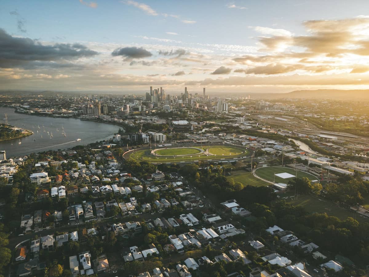 Weitläufige Luftaufnahme über Brisbane mit Vororten, Flussbiegungen, der Innenstadt-Skyline und der Moreton Bay in der Abenddämmerung.