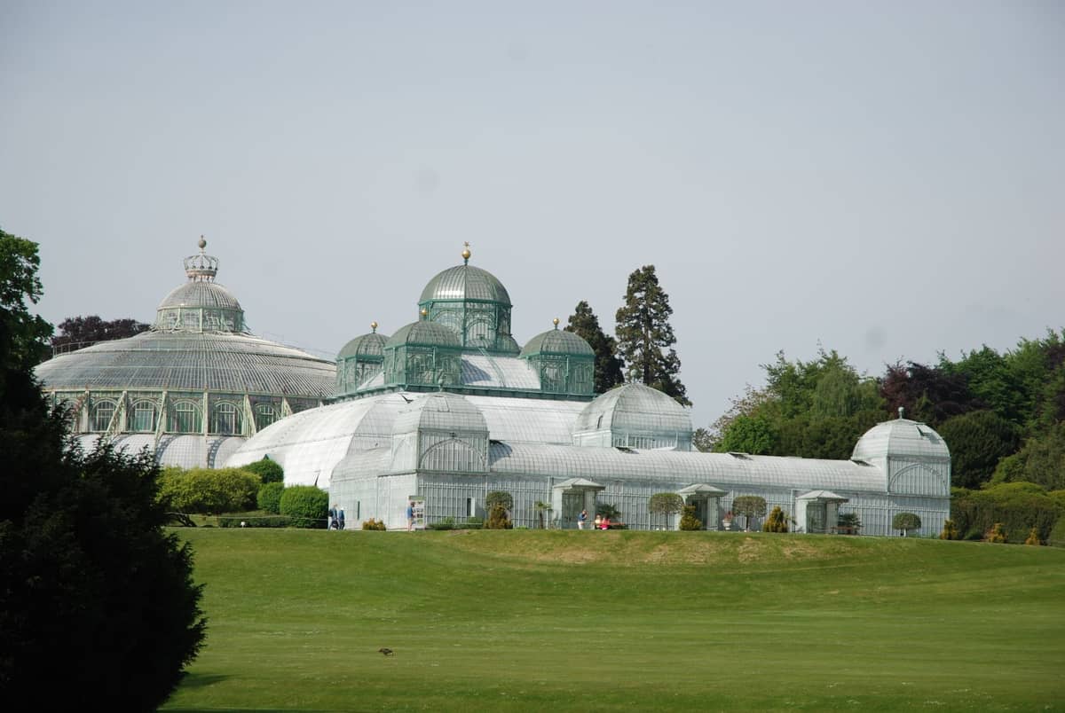 Vista panorâmica das Estufas Reais de Laeken, Bruxelas, com ornamentadas cúpulas de vidro rodeadas de gramados verdes e árvores.