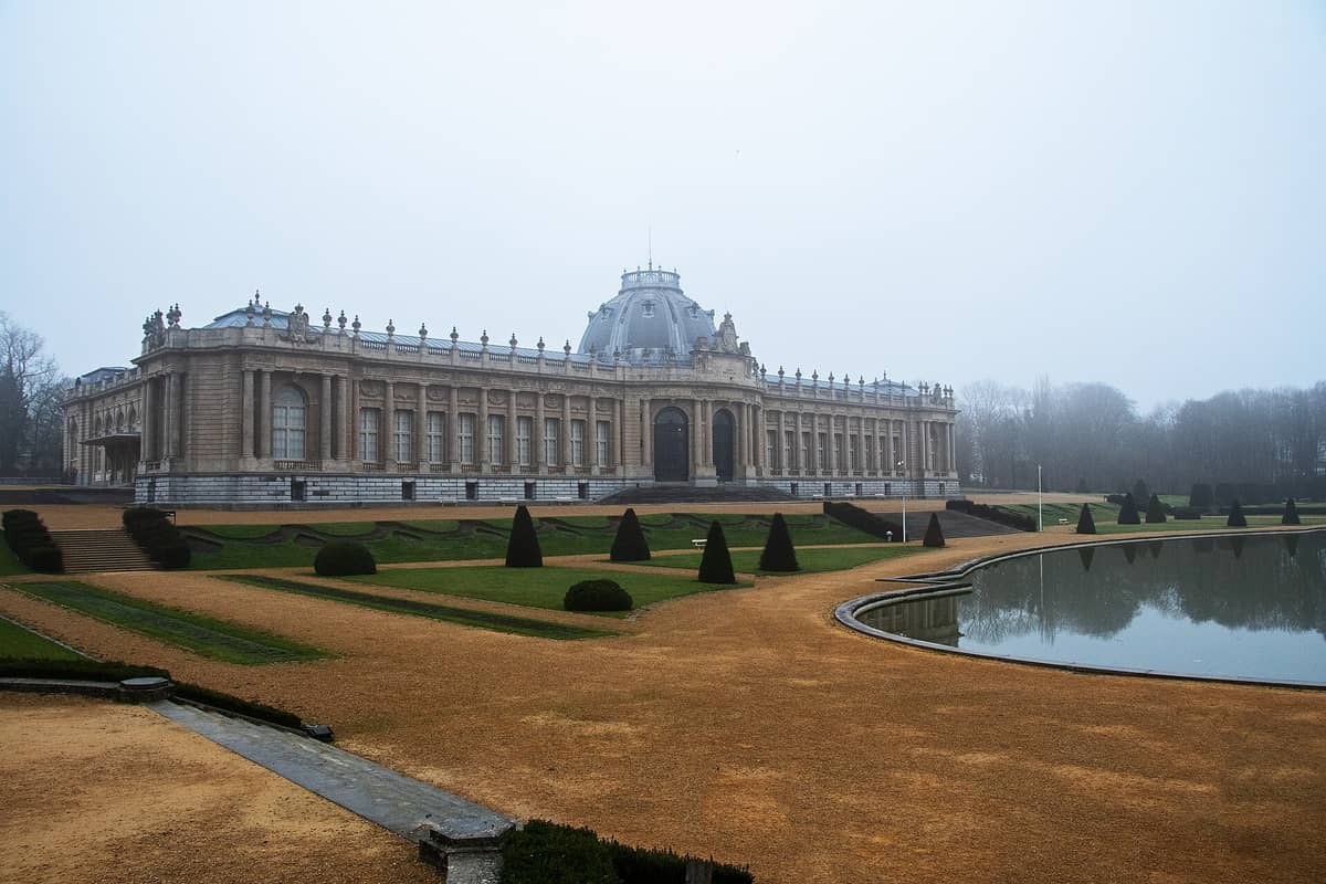 Vista ampla do Museu Real da África Central perto de Bruxelas, mostrando sua grande cúpula, jardins formais e um grande espelho d'água em um dia nebuloso.