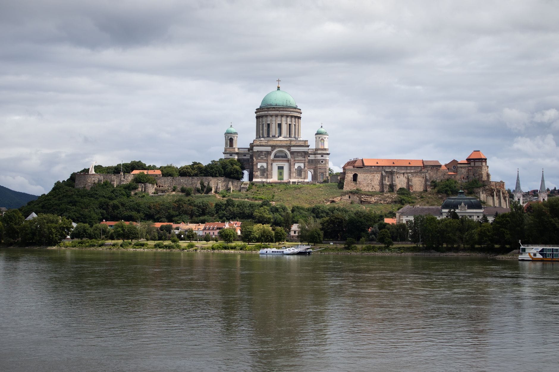 Bazylika w Esztergom i sąsiednie zabytkowe budowle widziane z drugiego brzegu Dunaju pod zachmurzonym niebem.