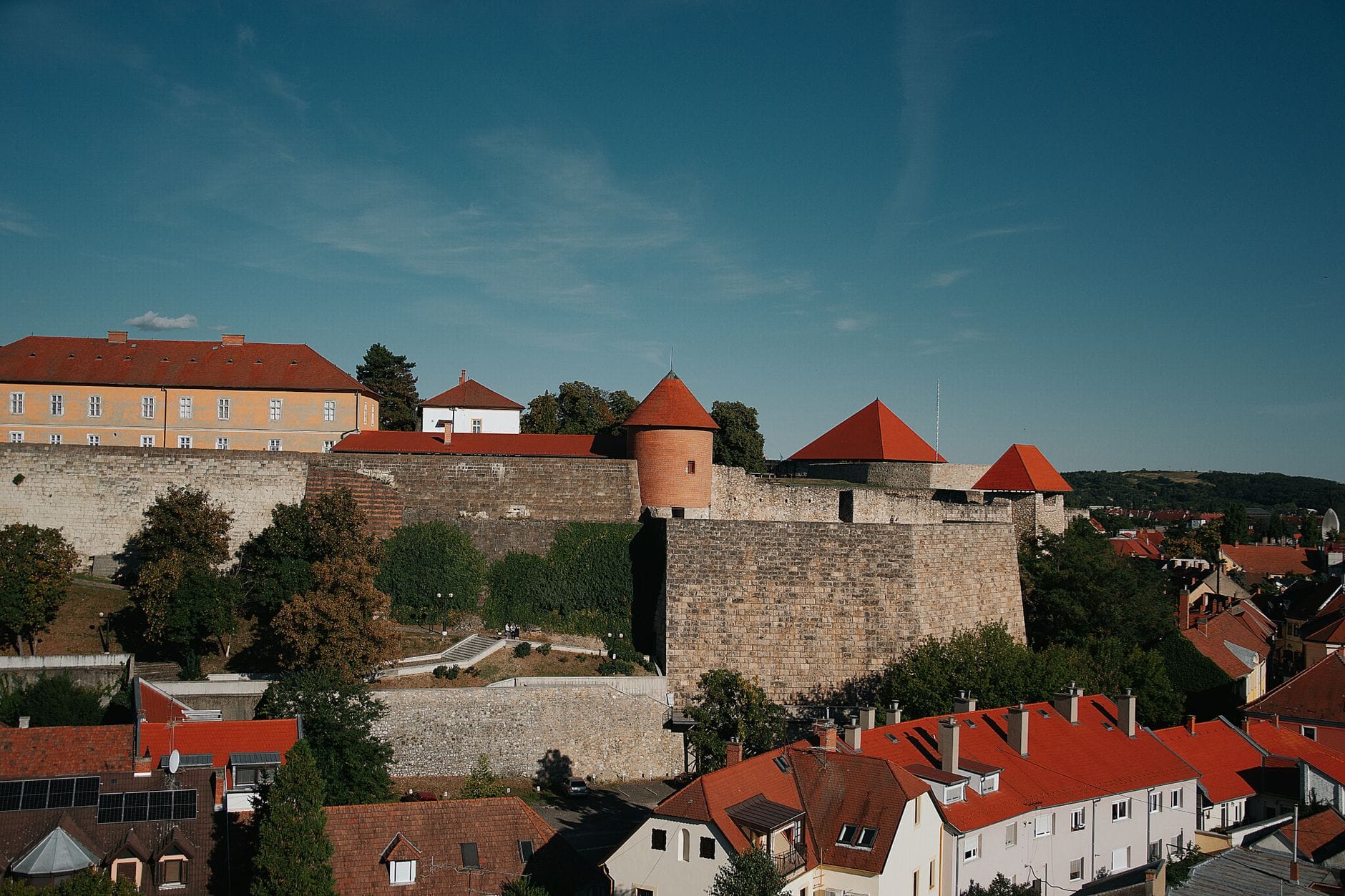 Panoramiczny widok na Zamek Eger z kamiennymi murami i wieżami z czerwonymi dachami wznoszącymi się ponad historycznym miastem i okolicznymi budynkami.