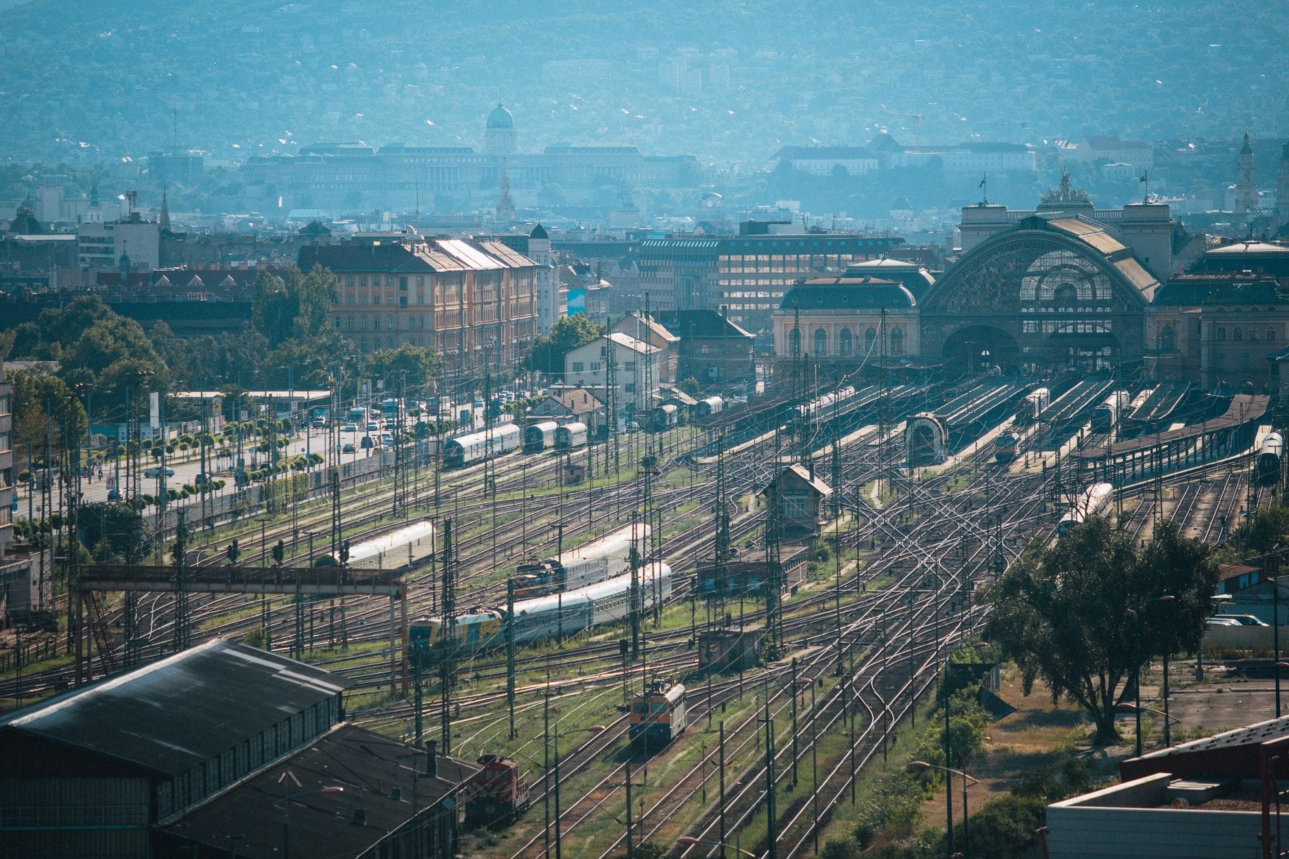 Szeroki widok na dworzec kolejowy Keleti w Budapeszcie z torami rozchodzącymi się na zewnątrz i panoramą miasta w tle.