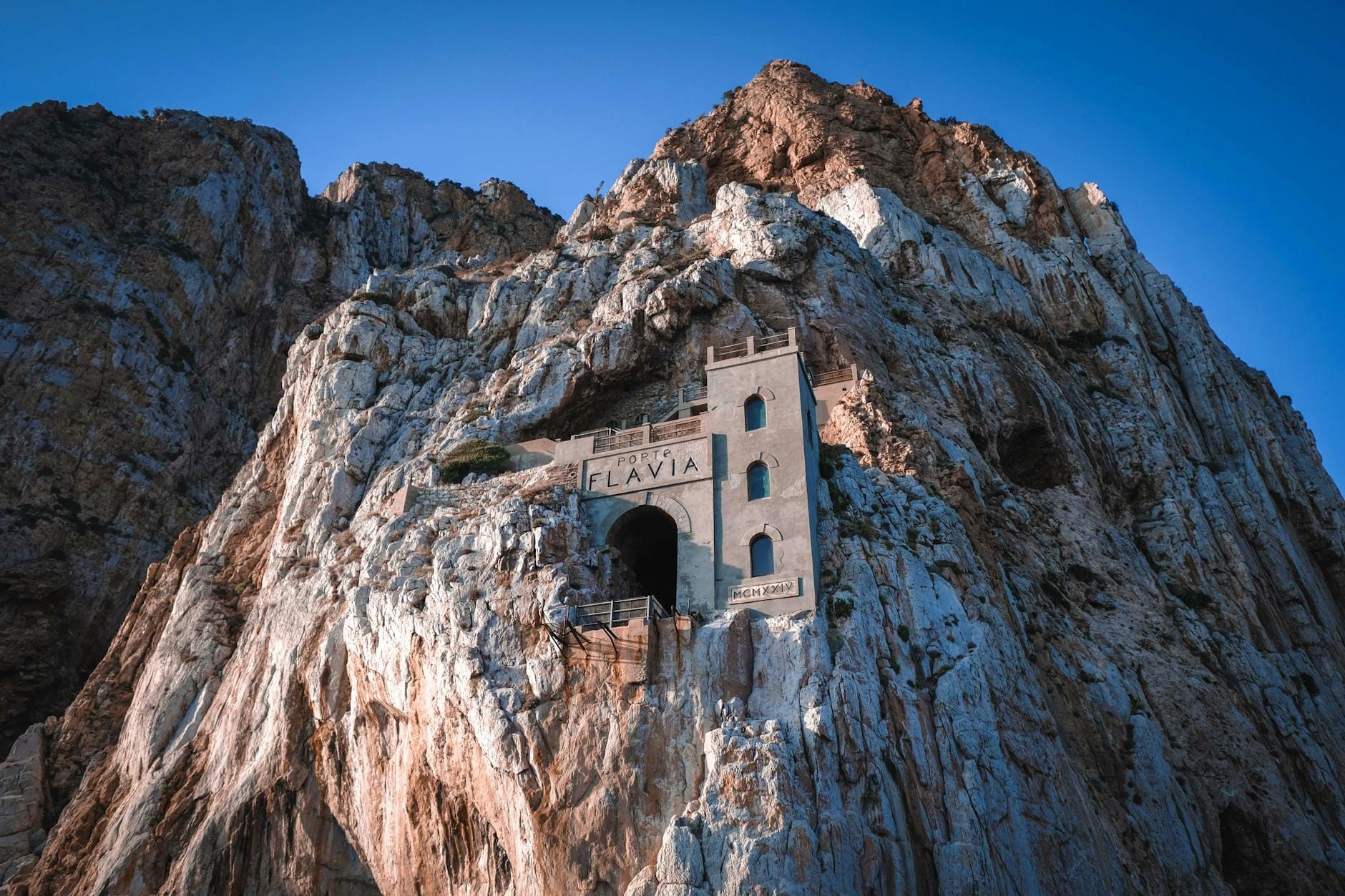 Historisches Bergbaugebäude in dramatischen Meeresfelsklippen, mit dem beleuchteten Eingang des Porto Flavia-Tunnels auf Sardinien.