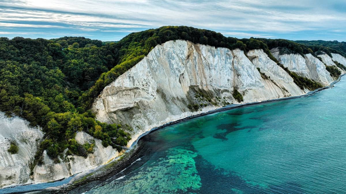 Dramatische weiße Kreidefelsen erheben sich über das türkisfarbene Meer mit einem üppigen grünen Wald auf dem Gipfel, aus der Vogelperspektive gesehen.
