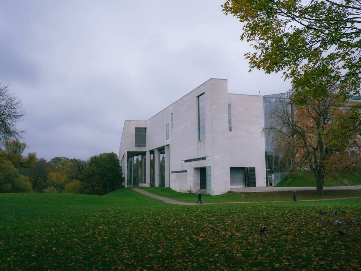 Ein modernes, hell gefärbtes Museumsgebäude befindet sich in einem üppigen Park unter einem bewölkten Himmel und deutet auf eine bedeutende Kunstinstitution außerhalb von Kopenhagen hin.