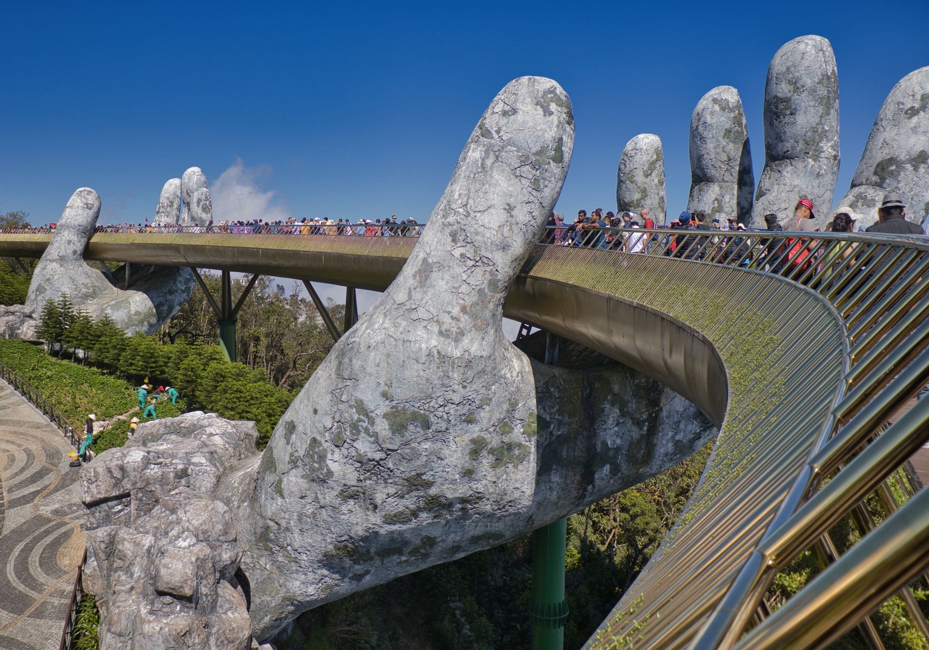 สะพาน Golden Bridge ที่ Ba Na Hills ถูกรองรับด้วยมือหินยักษ์ พร้อมนักท่องเที่ยวจำนวนมากและท้องฟ้าสีคราม