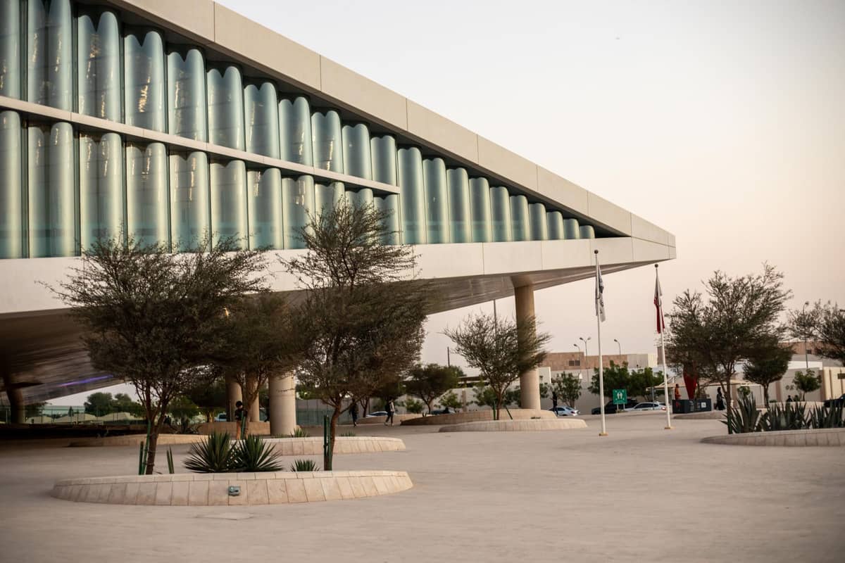Modernes Äußeres der Qatar National Library in Education City, Doha, mit Glaswänden und gestalteter Eingangszone in der Abenddämmerung.