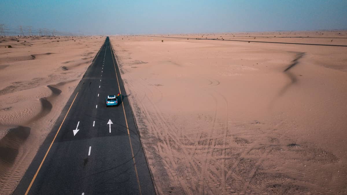 Eine lange, gerade Straße durch die Wüste der VAE mit einem einzelnen Auto – sinnbildlich für unabhängige Tagesausflüge von Dubai nach Abu Dhabi, Hatta und anderen Zielen.