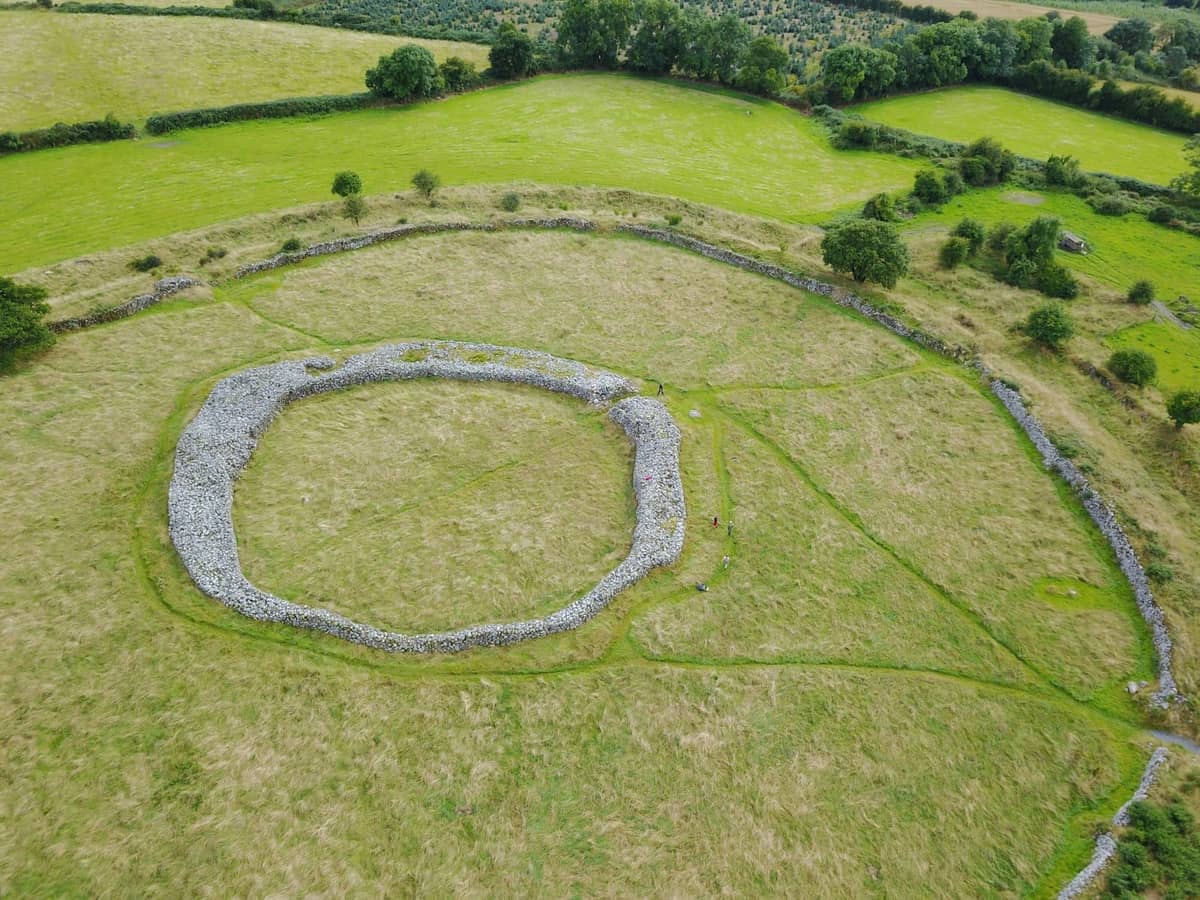 Vista aérea de un gran círculo de piedras prehistórico o fuerte anular en un campo herboso rodeado de un ondulado paisaje verde.