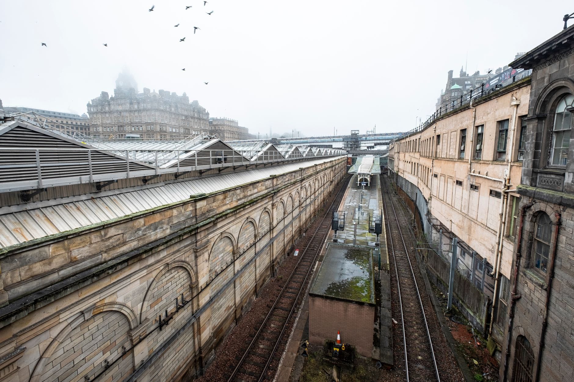 Binari ferroviari in ingresso alla stazione di Edinburgh Waverley con edifici storici e banchine visibili in una giornata nuvolosa.