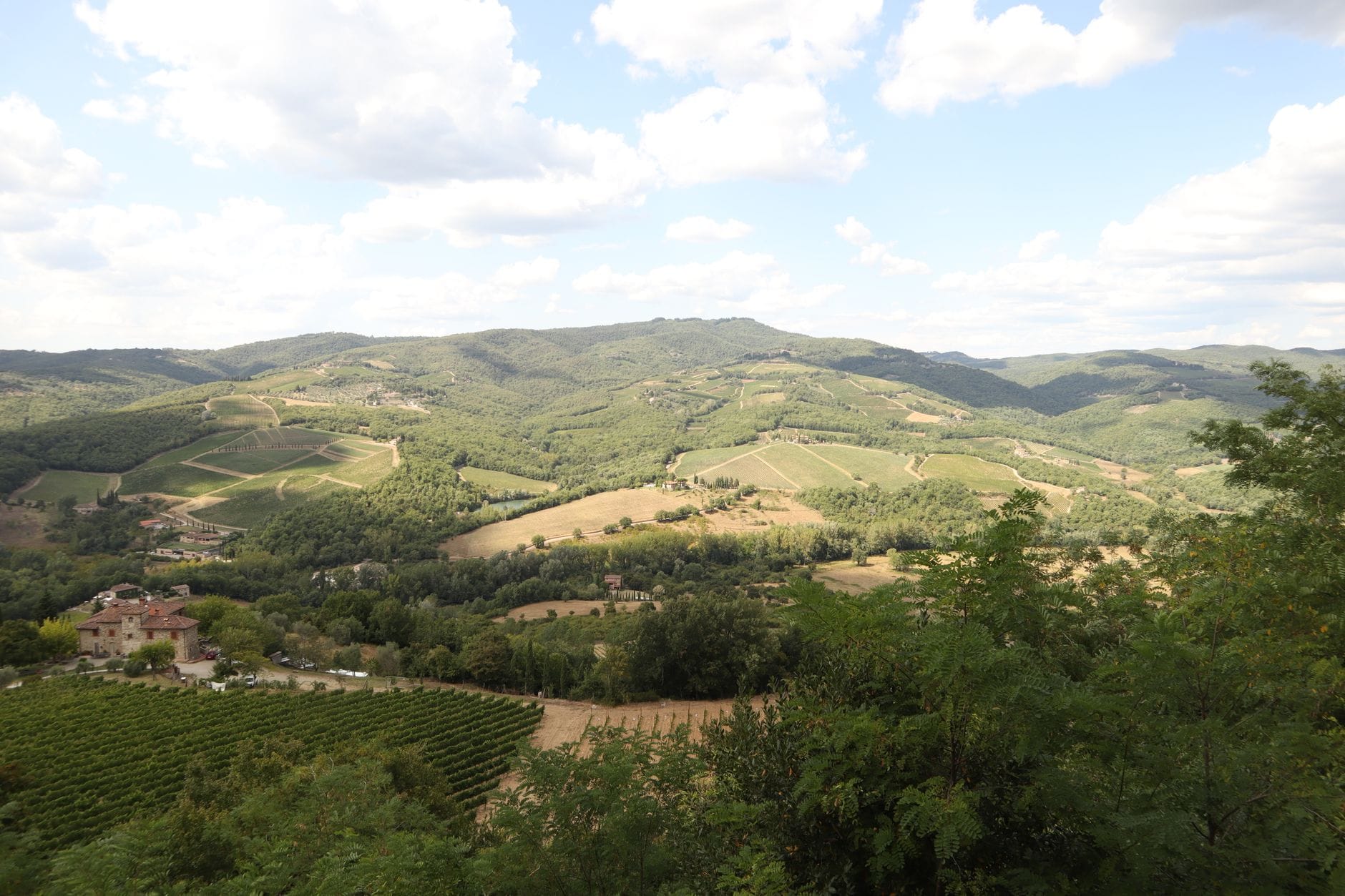 วิวเนินเขาสีเขียวที่ลูกคลื่น ไร่องุ่น และทุ่งนาหลากสีของ Chianti ใน Tuscany ภายใต้ท้องฟ้ามีเมฆบางส่วน