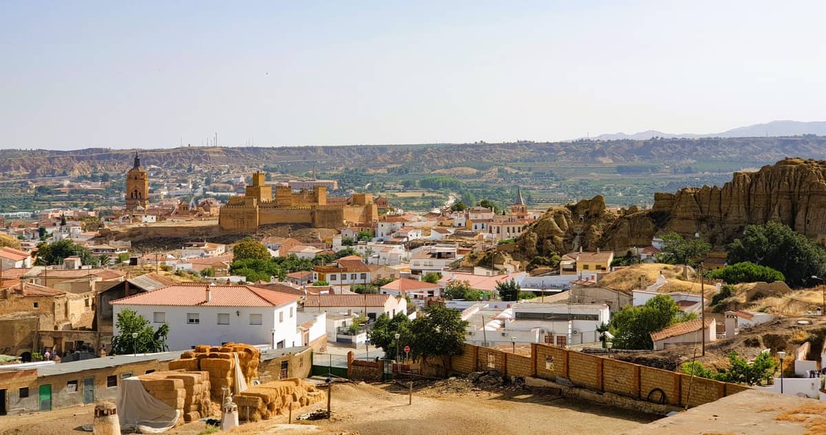 วิวพาโนรามาของ Guadix แสดงให้เห็นบ้านถ้ำ อาคารประวัติศาสตร์ เนินเขาหินผา และมหาวิหารภายใต้ท้องฟ้าแจ่มใส