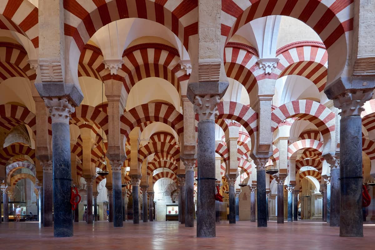 วิวกว้างของซุ้มโค้งและเสาลายแถบสีแดงและขาวอันโดดเด่นภายใน Mezquita-Catedral ในเมืองกอร์โดบา ประเทศสเปน พร้อมมุมมองสมมาตรแบบเปิด