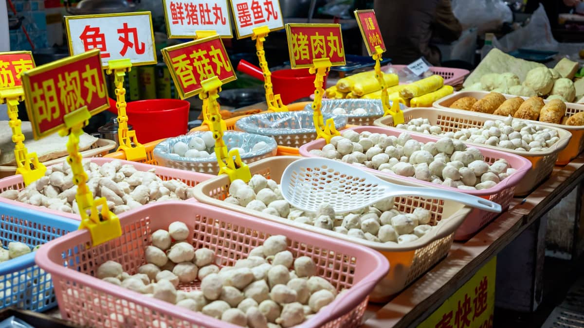Street food market stall with baskets of assorted Cantonese fish and meat balls labeled in Chinese characters.