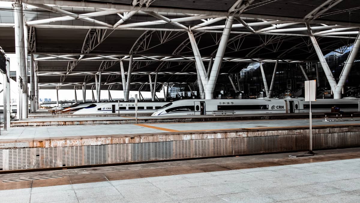 Wide view of a modern high-speed rail station with sleek white bullet trains at the platforms under a large steel canopy.