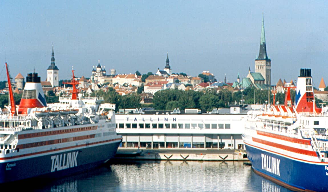 Ferries da Tallink atracados no porto com a Cidade Velha medieval de Tallinn visível ao fundo, incluindo torres de igrejas e telhados vermelhos.