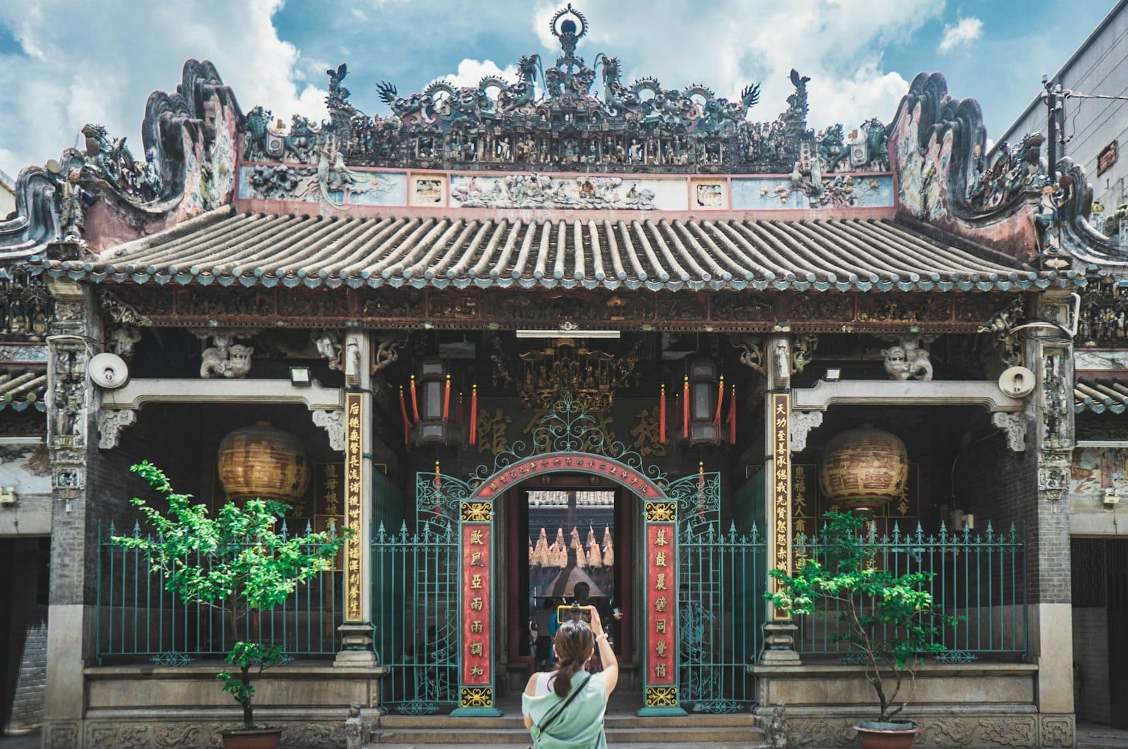 Vista frontal de un templo histórico ricamente decorado con techo ornamentado, linternas rojas y un turista tomando una foto en Ho Chi Minh City.