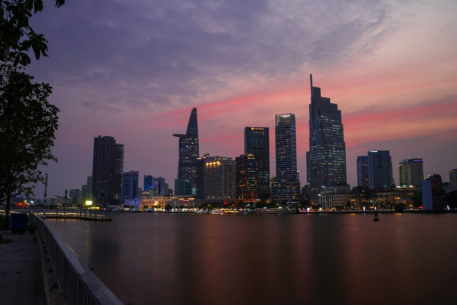 Horizonte de Ho Chi Minh City al anochecer con la Bitexco Tower y otros edificios modernos reflejados en el río bajo un cielo colorido.