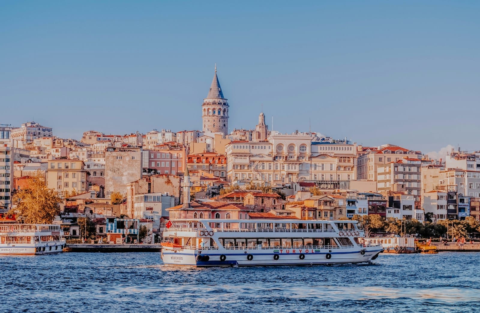 Vista panorâmica de Istambul com a Torre Gálata, prédios históricos e balsas no Bósforo sob um céu azul e limpo.