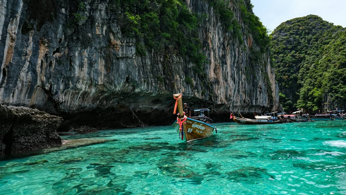Bote de cola larga acercándose a los dramáticos acantilados de piedra caliza y las aguas turquesas de las Islas Phi Phi cerca de Krabi, con vegetación exuberante y cielo azul despejado.