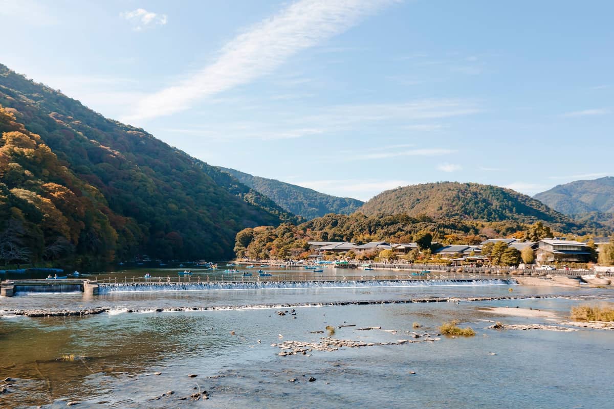 Wide landscape view of Arashiyama’s mountains, the Katsura River, and the iconic Togetsukyo Bridge on a clear, sunny day near Kyoto.