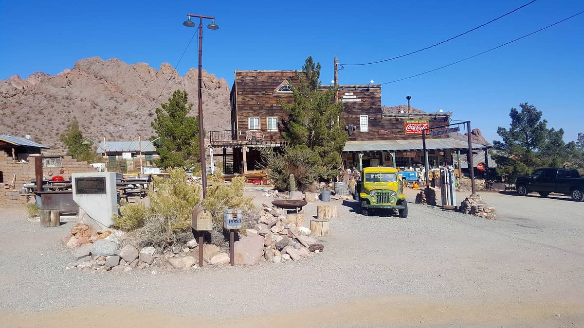Edificio de madeira clássico no estilo do Velho Oeste com veículos antigos e montanhas desérticas em Nelson Ghost Town perto de Las Vegas, Nevada, sob um céu azul limpo.