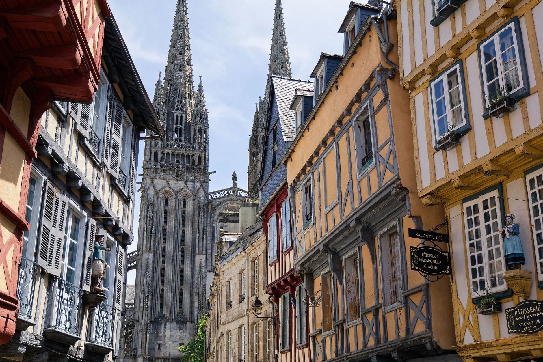 Rumah-rumah bergaya setengah kayu abad pertengahan berjajar di sepanjang jalan sempit, dengan menara-menara Cathédrale de Rouen menjulang dramatis di latar belakang.
