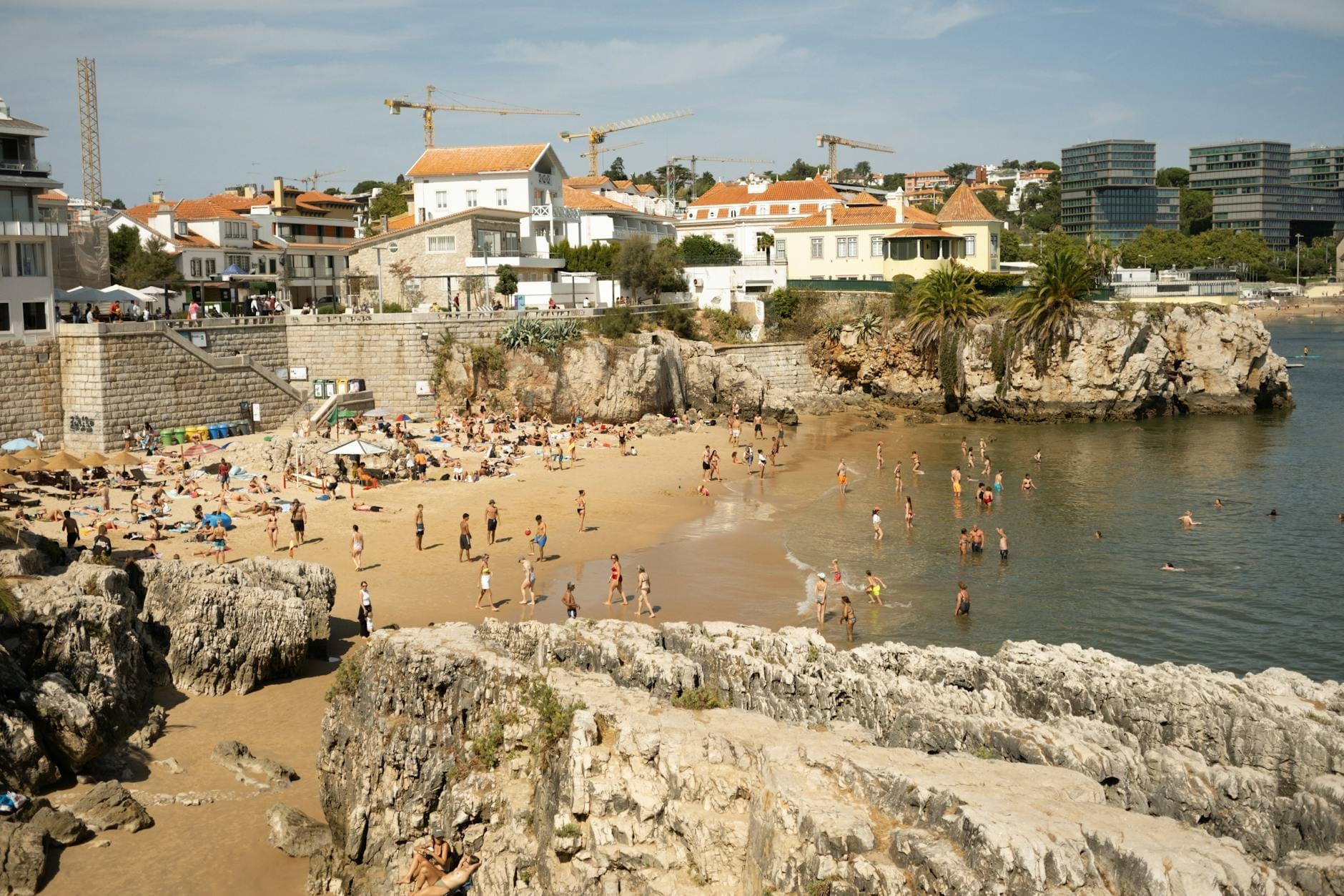Plage animée à Cascais avec des baigneurs, des falaises rocheuses et des maisons historiques, illustrant le charme balnéaire de la Ligne de Cascais.