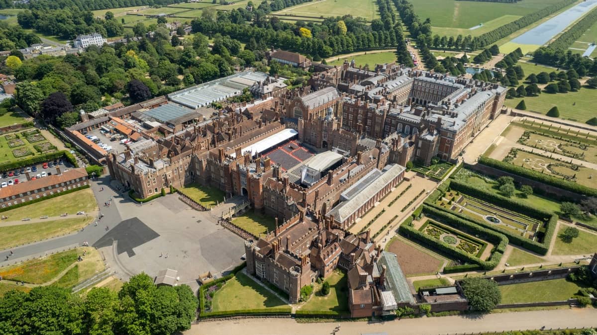 Vista aérea do Hampton Court Palace e seus jardins formais, rodeados de árvores e parques no vale do Tâmisa perto de Londres.