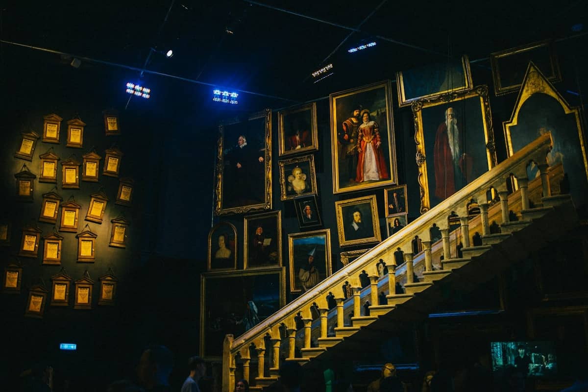 Uma escadaria ladeada de retratos iluminados no interior do Harry Potter Studio Tour, com decoração mágica icônica e uma atmosfera envolvente.