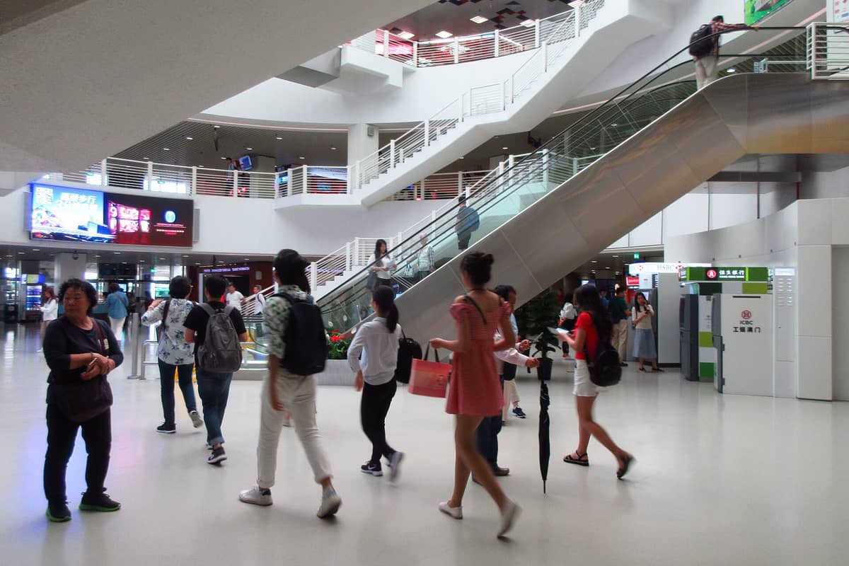 Passagiere im modernen Innenbereich des Shenzhen Shekou Ferry Terminal, mit Rolltreppen und umherlaufenden Menschen.