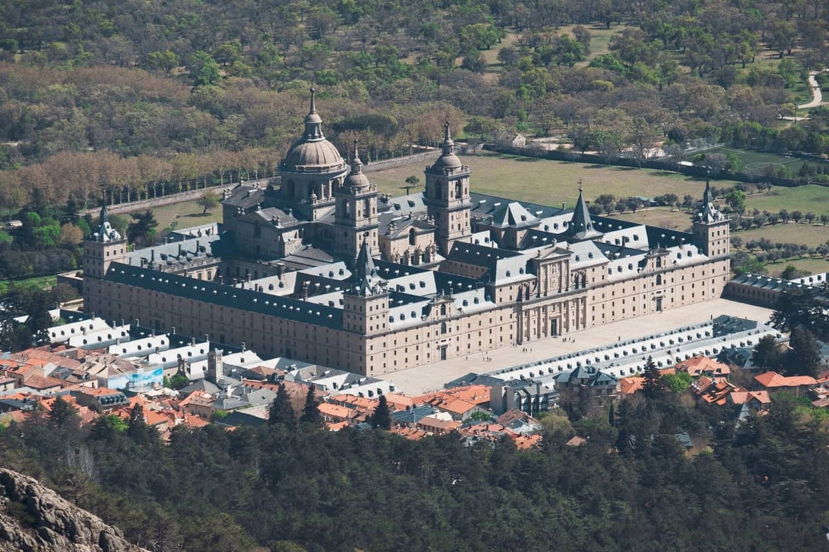 Luftaufnahme des prächtigen El Escorial-Komplexes, umgeben von Grünflächen und kleinen Dächern, die seine monumentale Renaissance-Architektur zur Geltung bringt.