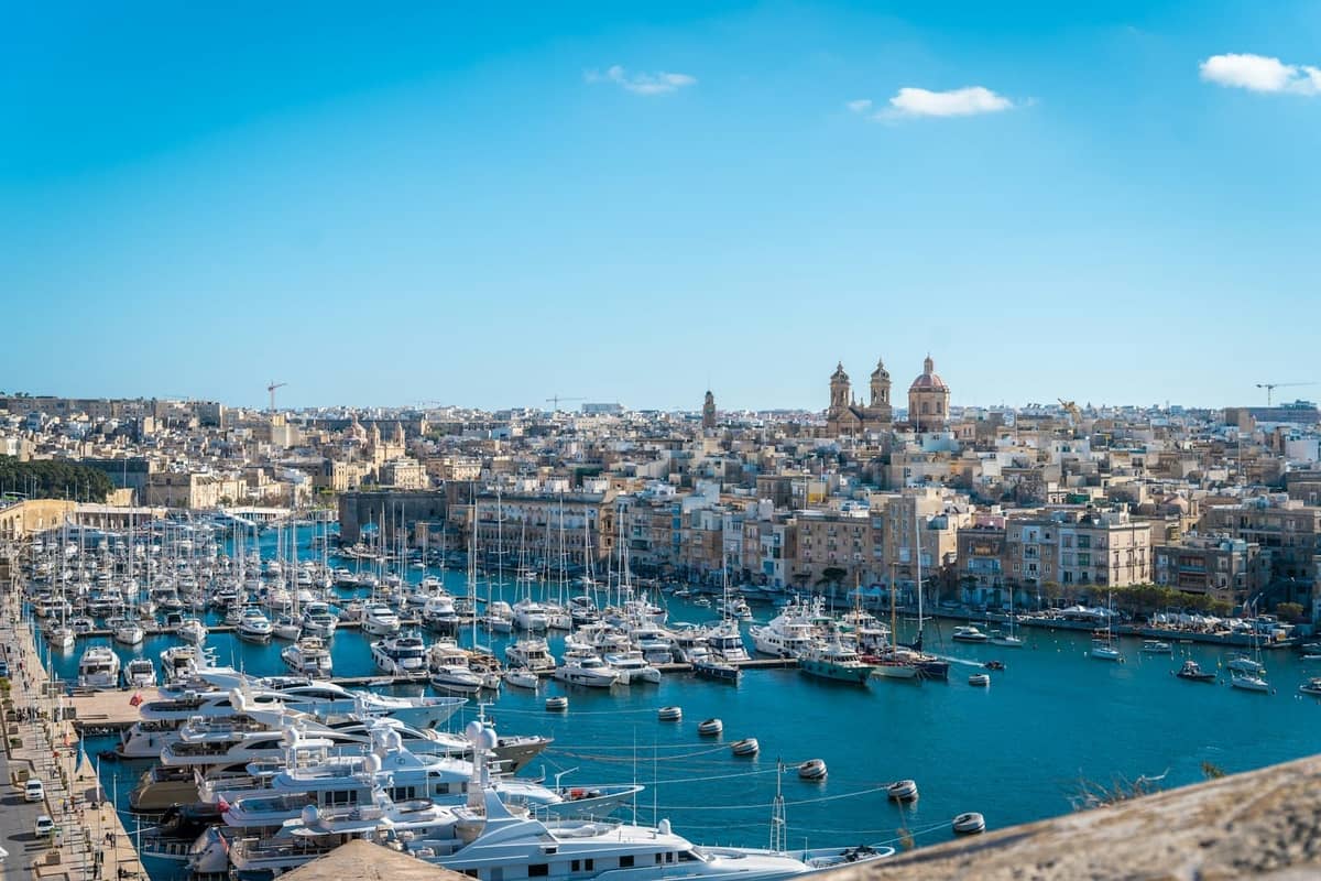 Panoramablick auf die historischen Three Cities Maltas mit einem von Yachten gefüllten Yachthafen und ikonischen Kirchenkuppeln im Hintergrund unter einem klaren blauen Himmel.