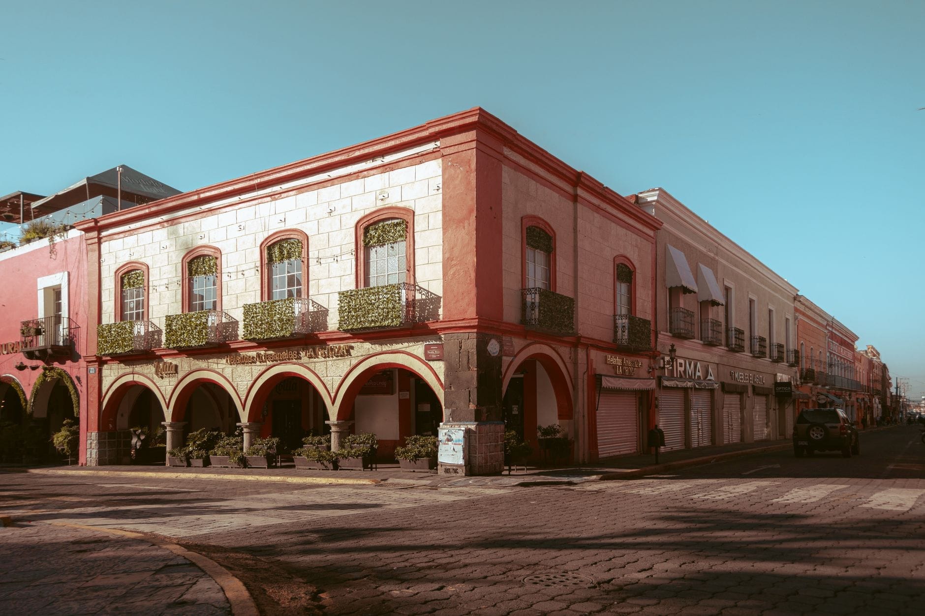 Edifício da época colonial com arcos e varandas em uma esquina iluminada pelo sol, típico da arquitetura das cidades mexicanas.