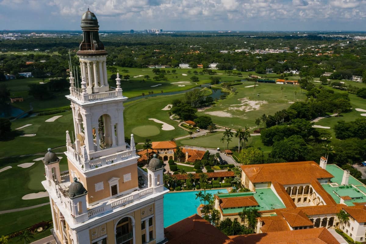 Aerial view of the iconic Biltmore Hotel in Coral Gables with Mediterranean Revival architecture, golf course, and surrounding greenery.
