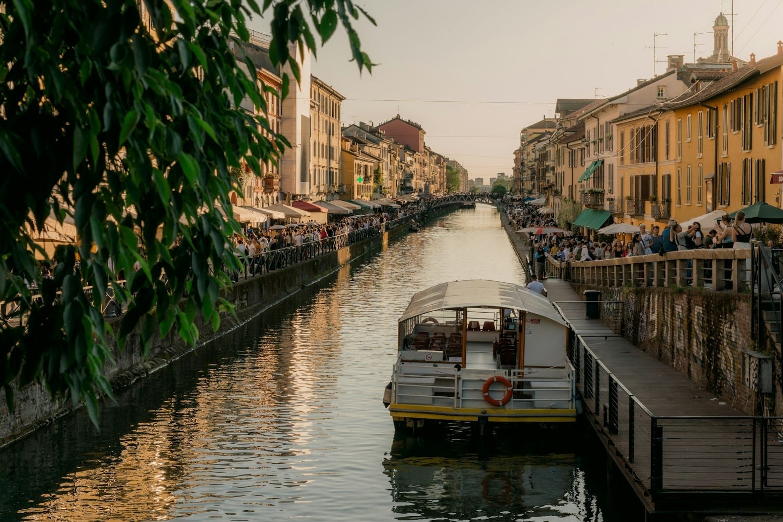 Cena de canal ao pôr do sol com um barco, calçadão animado e fileiras de casas coloridas, capturando o charme dos destinos de passeio de um dia facilmente acessíveis a partir de Milão.