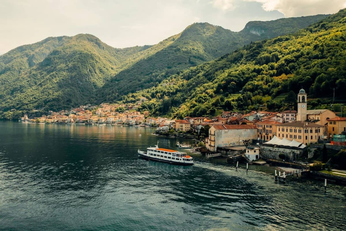 Ferry boat arriving at a picturesque lakeside town with orange-roofed buildings, nestled between green mountains and the calm waters of an Italian lake.