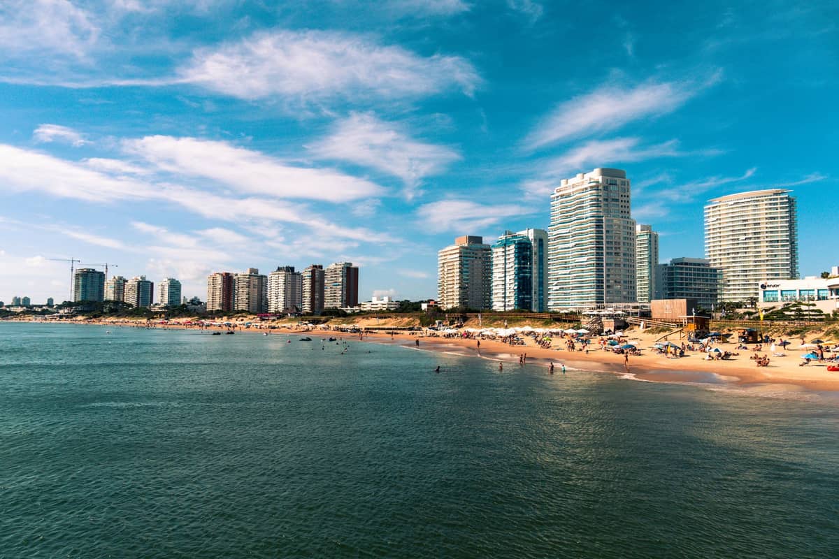 วิวพาโนรามาของชายหาด Punta del Este พร้อมอาคารสูงสมัยใหม่ ชายฝั่งทรายขาว และผู้คนที่สนุกสนานกับน้ำในวันที่แดดจัด