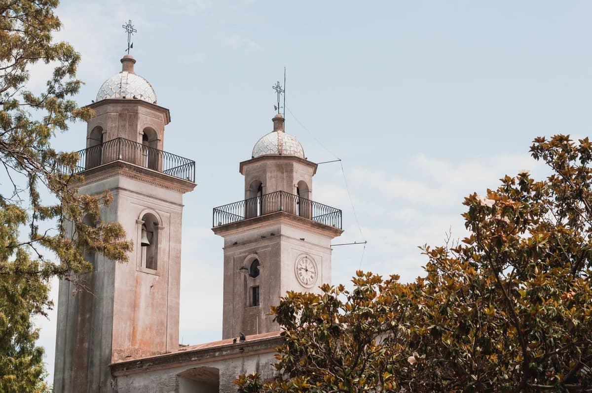 หอระฆังคู่ของ Basilica del Santísimo Sacramento โดดเด่นเหนือต้นไม้ใบหนาแน่นใน Colonia del Sacramento ภายใต้ท้องฟ้าแจ่มใสในเวลากลางวัน