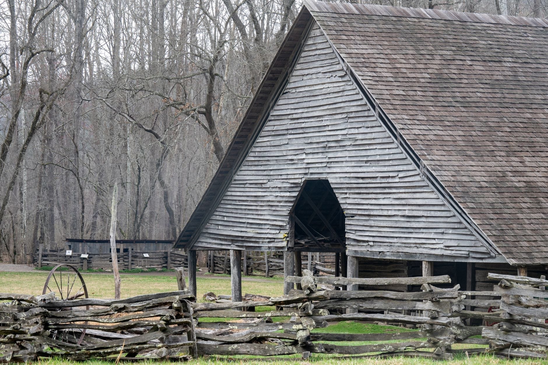 Granero histórico de madera con cerca de rieles partidos al frente y árboles sin hojas al fondo, evocando un entorno rural del Tennessee del siglo XIX.