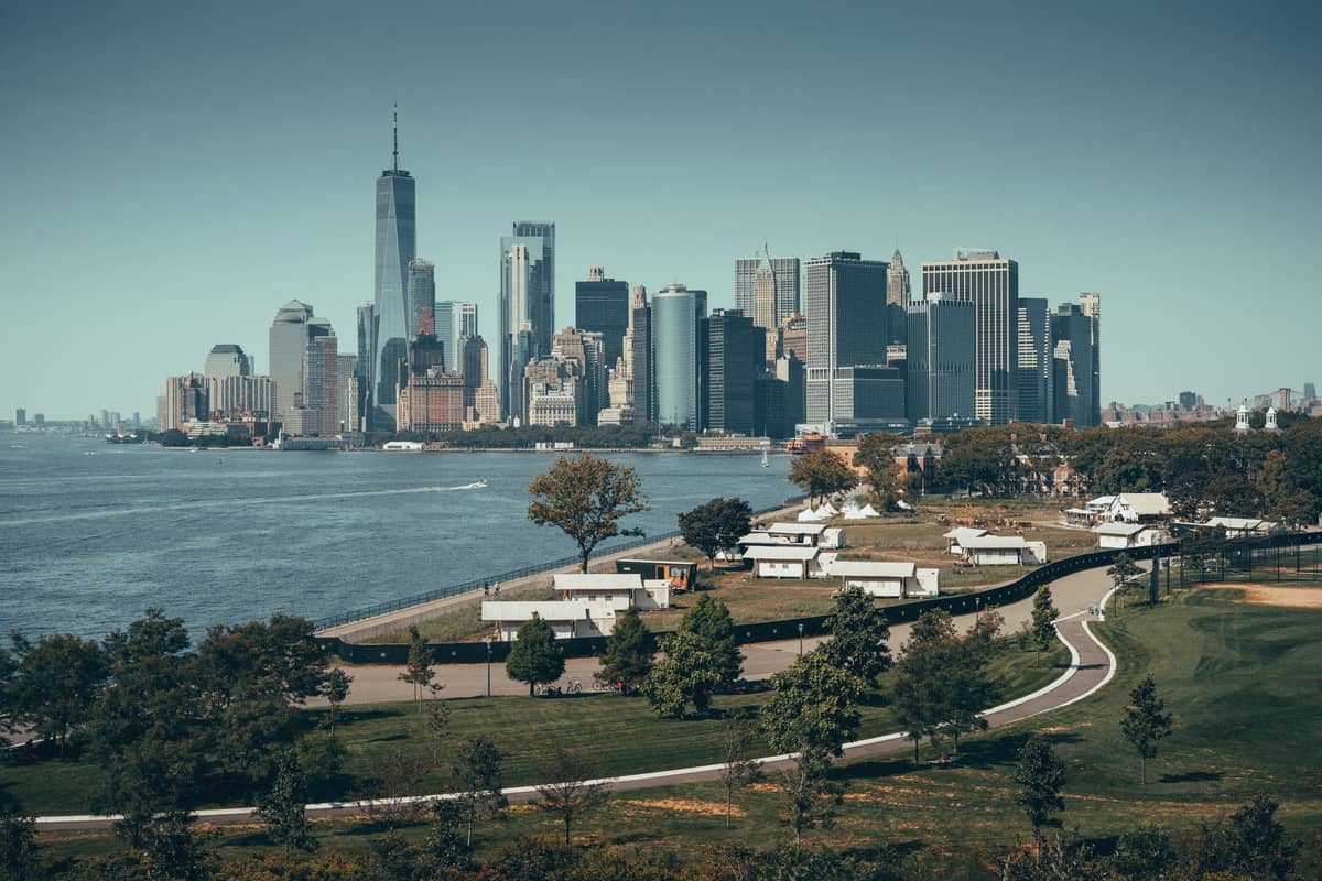 Weite Aussicht auf Governors Island im Vordergrund mit der Skyline von Lower Manhattan auf der anderen Seite des Hafens im Hintergrund an einem klaren Tag.
