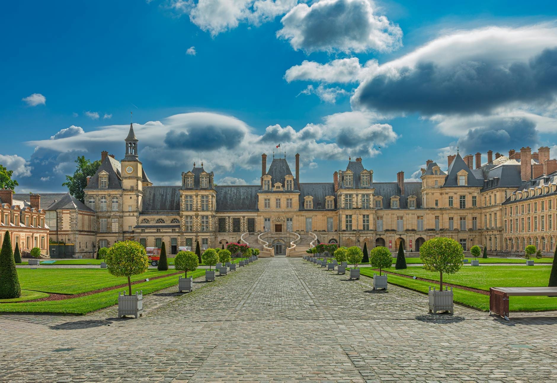 Château de Fontainebleau'nun bakımlı bahçeleri, süslü mimarisi ve üzerindeki dramatik bulutlarıyla geniş ve simetrik görünümü